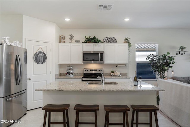 kitchen featuring white cabinets, a kitchen island with sink, light stone counters, and appliances with stainless steel finishes