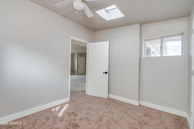 unfurnished room with a skylight, light carpet, and ceiling fan