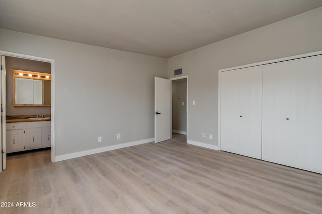 unfurnished bedroom with light wood-type flooring, connected bathroom, a closet, and sink