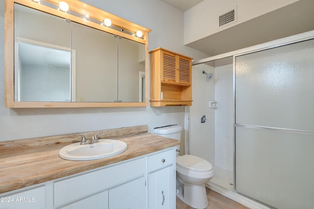 bathroom with wood-type flooring, vanity, toilet, and a shower with door