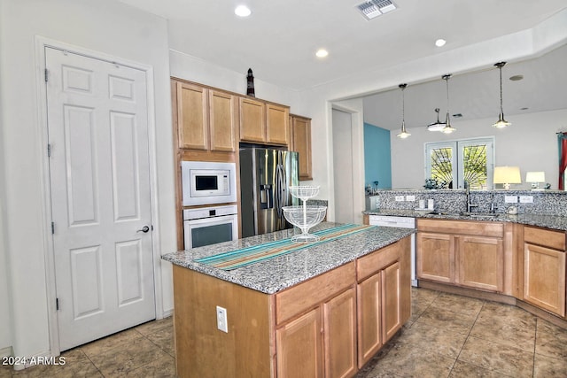 kitchen featuring stone counters, sink, decorative light fixtures, white appliances, and a kitchen island