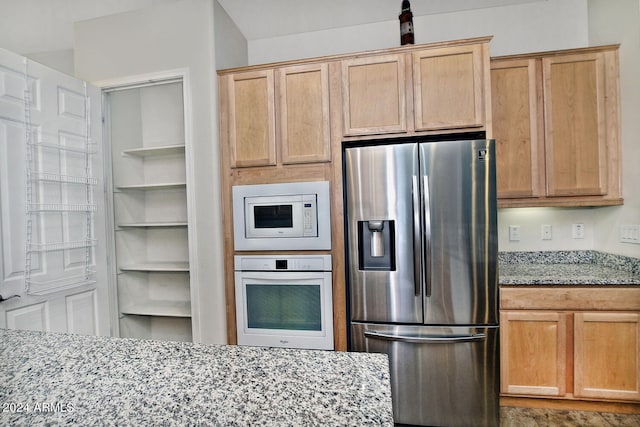 kitchen with light stone countertops, light brown cabinets, built in features, and white appliances