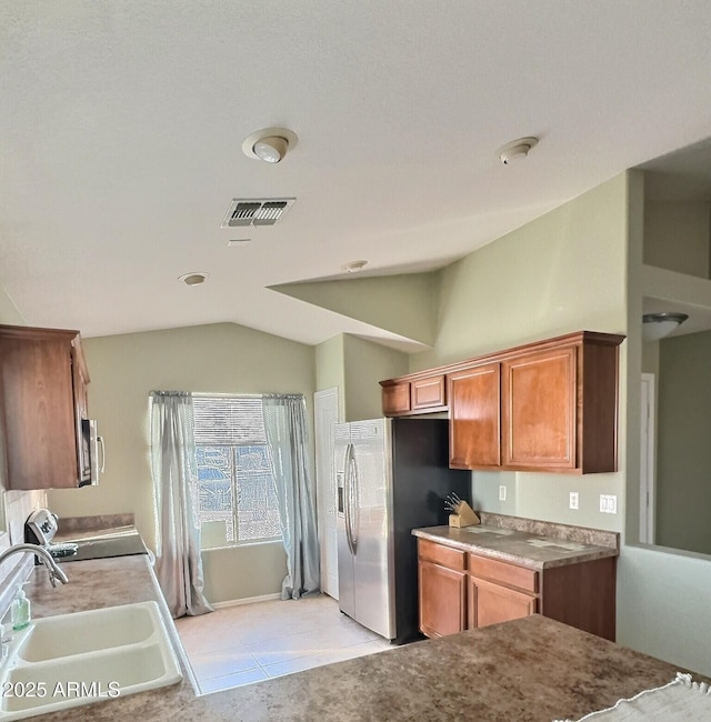 kitchen with visible vents, brown cabinetry, stainless steel appliances, vaulted ceiling, and a sink