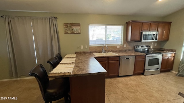 kitchen featuring a breakfast bar area, light tile patterned floors, appliances with stainless steel finishes, a sink, and a peninsula