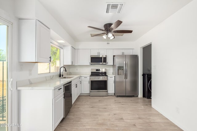 kitchen with visible vents, white cabinets, light wood-style flooring, stainless steel appliances, and a sink