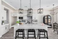 kitchen featuring a breakfast bar area, white cabinetry, an island with sink, and pendant lighting