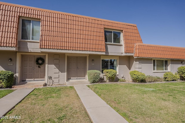 view of property featuring a front lawn, mansard roof, a tile roof, and brick siding