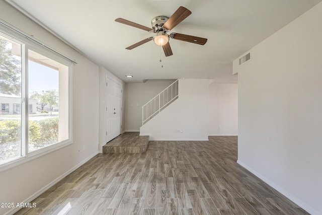 unfurnished living room with baseboards, visible vents, a ceiling fan, wood finished floors, and stairs