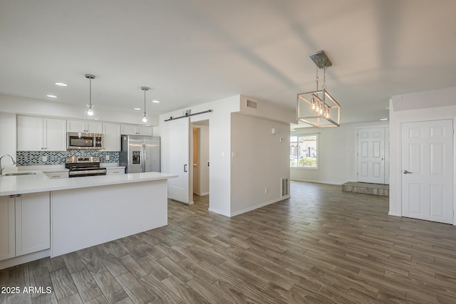 kitchen with a barn door, stainless steel appliances, a peninsula, a sink, and tasteful backsplash