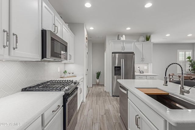 kitchen with sink, backsplash, white cabinets, light hardwood / wood-style floors, and stainless steel appliances