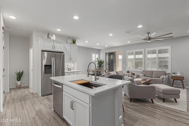 kitchen featuring white cabinetry, sink, light hardwood / wood-style floors, stainless steel appliances, and a center island with sink