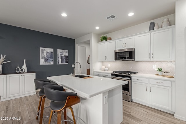 kitchen featuring sink, light wood-type flooring, appliances with stainless steel finishes, a kitchen island with sink, and white cabinets