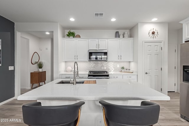 kitchen with sink, white cabinetry, appliances with stainless steel finishes, a kitchen island with sink, and backsplash