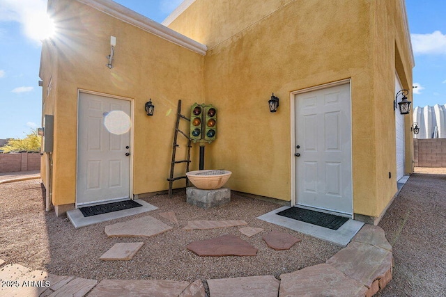 entrance to property featuring fence and stucco siding
