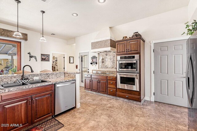 kitchen with hanging light fixtures, light stone counters, a sink, stainless steel appliances, and custom exhaust hood