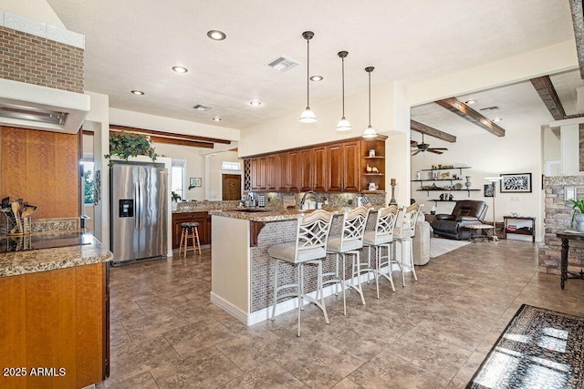 kitchen featuring brown cabinetry, visible vents, a peninsula, a kitchen breakfast bar, and stainless steel refrigerator with ice dispenser