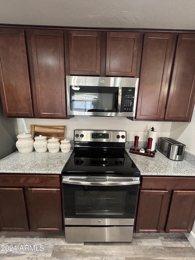 kitchen featuring light stone counters, dark brown cabinets, and appliances with stainless steel finishes