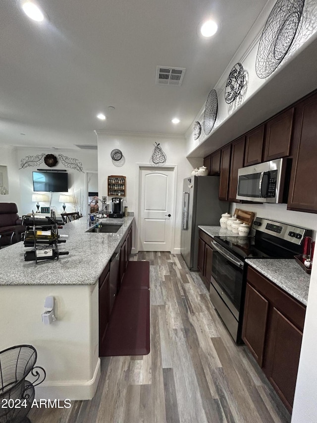 kitchen with dark brown cabinetry, sink, stainless steel appliances, light stone counters, and hardwood / wood-style flooring