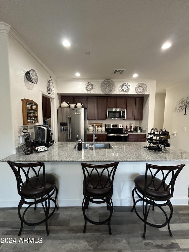 kitchen featuring dark brown cabinetry, sink, stainless steel appliances, dark wood-type flooring, and kitchen peninsula