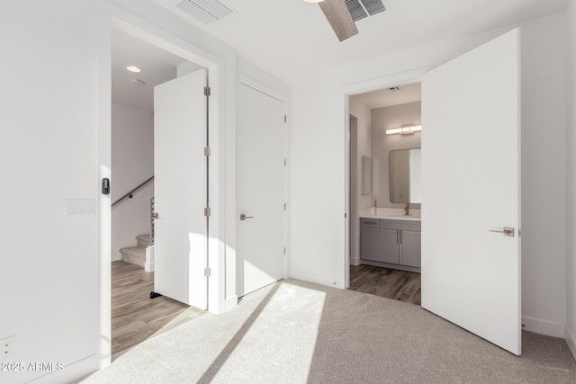 unfurnished bedroom featuring ceiling fan, sink, light colored carpet, and ensuite bath