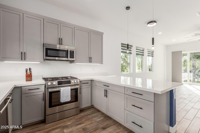 kitchen with decorative light fixtures, wood-type flooring, stainless steel appliances, gray cabinets, and kitchen peninsula