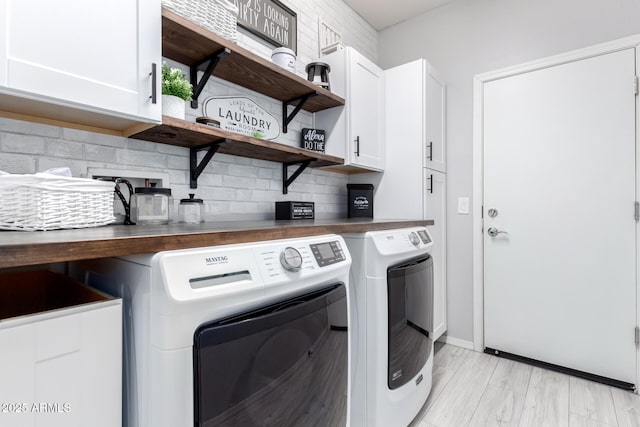 clothes washing area with cabinets, washing machine and dryer, and light wood-type flooring