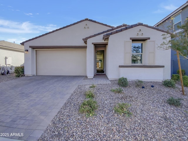 mediterranean / spanish house featuring a tiled roof, stucco siding, an attached garage, and decorative driveway