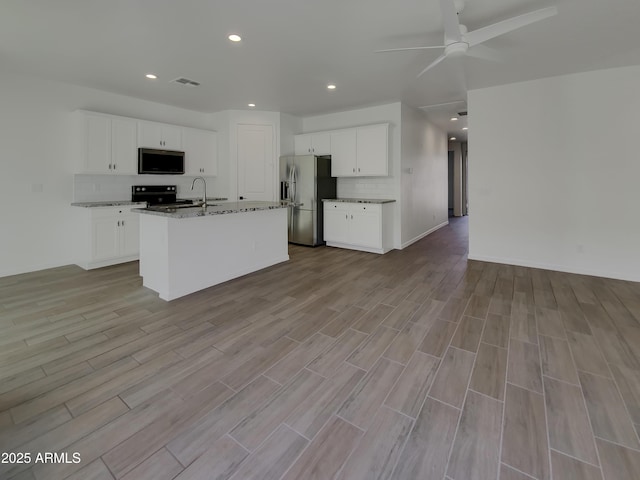 kitchen with a ceiling fan, light stone counters, tasteful backsplash, open floor plan, and stainless steel appliances