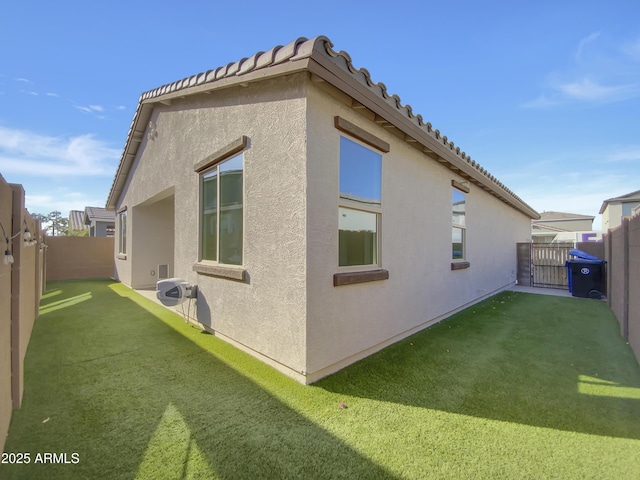 view of side of property with a yard, stucco siding, a tiled roof, and a fenced backyard