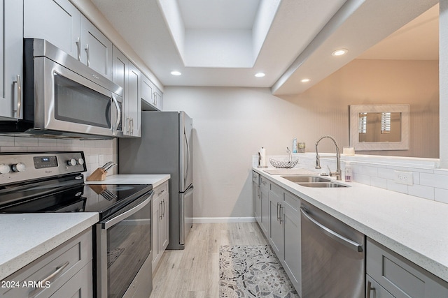 kitchen with decorative backsplash, light hardwood / wood-style floors, gray cabinets, stainless steel appliances, and sink