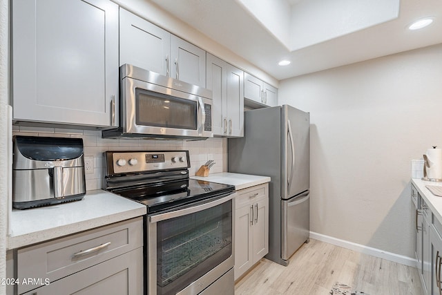 kitchen with light hardwood / wood-style flooring, backsplash, appliances with stainless steel finishes, and gray cabinets