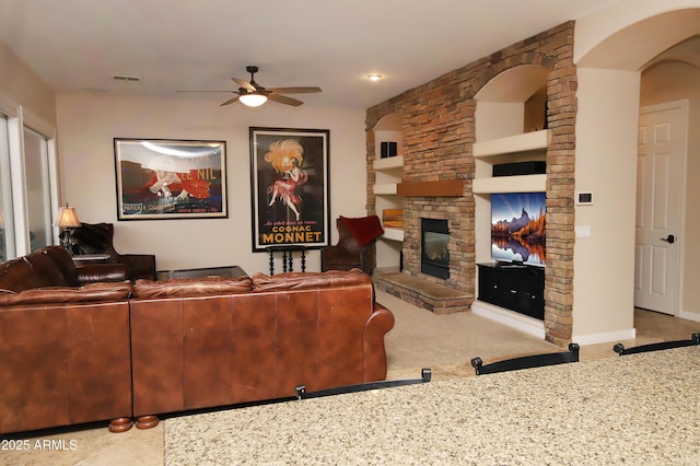 living room with ceiling fan, a stone fireplace, visible vents, and baseboards