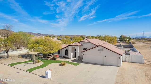 mediterranean / spanish home featuring a tile roof, stucco siding, a mountain view, fence, and a garage