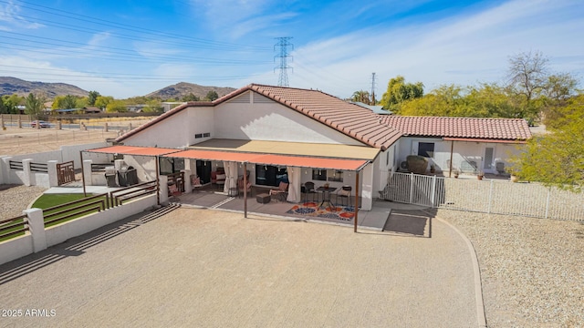 back of house with fence, a mountain view, and a tiled roof