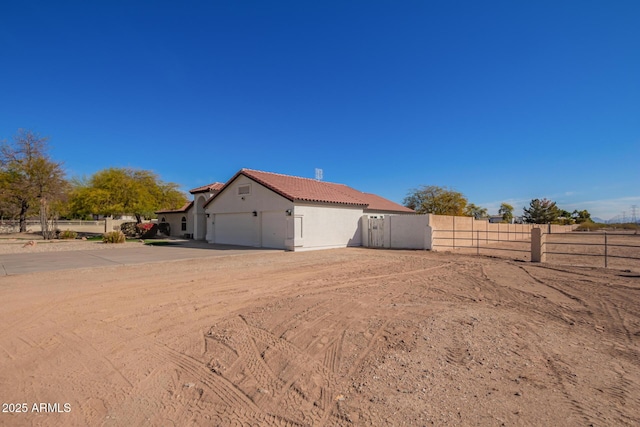 view of side of home featuring driveway, a garage, a tiled roof, fence, and stucco siding