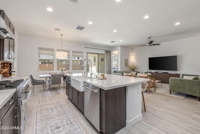 kitchen with decorative light fixtures, ceiling fan, a kitchen island with sink, appliances with stainless steel finishes, and sink