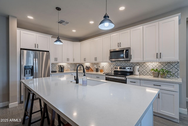 kitchen featuring pendant lighting, white cabinets, stainless steel appliances, sink, and a center island with sink