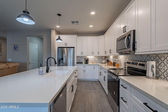 kitchen featuring appliances with stainless steel finishes, light wood-type flooring, pendant lighting, white cabinets, and sink