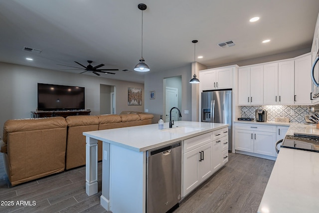 kitchen featuring white cabinets, appliances with stainless steel finishes, an island with sink, sink, and hanging light fixtures