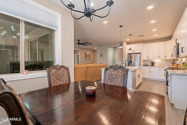 dining area with light hardwood / wood-style floors, ceiling fan with notable chandelier, and sink