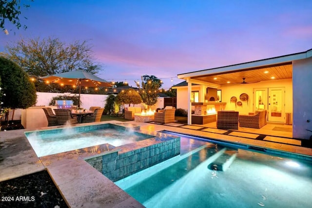 pool at dusk featuring an outdoor living space with a fireplace, pool water feature, ceiling fan, an in ground hot tub, and a patio