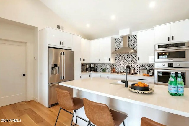 kitchen with a kitchen bar, appliances with stainless steel finishes, light wood-type flooring, wall chimney range hood, and white cabinetry