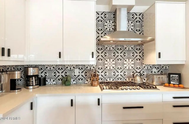 kitchen with decorative backsplash, white cabinets, wall chimney range hood, and stainless steel gas cooktop