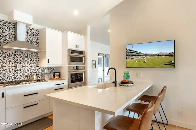 kitchen with white cabinetry, sink, wall chimney exhaust hood, stainless steel appliances, and a breakfast bar