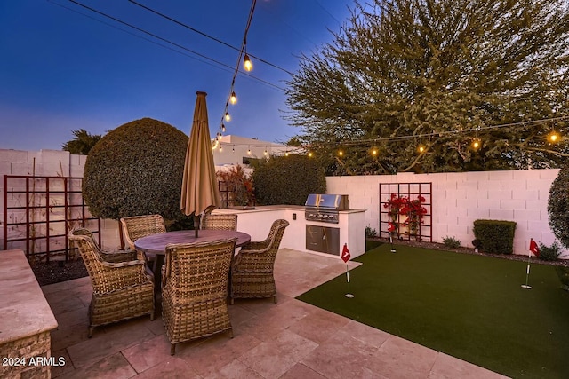 patio terrace at dusk featuring a grill and an outdoor kitchen