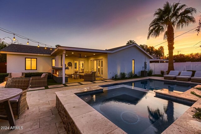 pool at dusk featuring an in ground hot tub, an outdoor living space, a patio, and ceiling fan