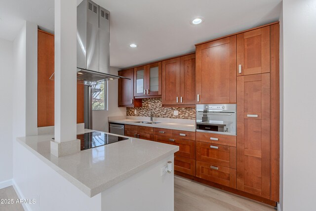 kitchen featuring island exhaust hood, a sink, stainless steel appliances, brown cabinetry, and tasteful backsplash