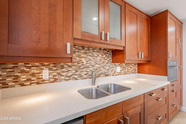 kitchen featuring a sink, brown cabinetry, stainless steel oven, light countertops, and decorative backsplash