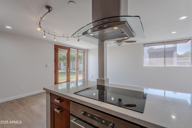 kitchen featuring light wood finished floors, island exhaust hood, oven, light countertops, and black electric stovetop