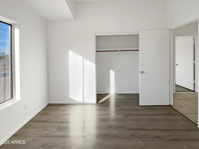 unfurnished bedroom with multiple windows, dark hardwood / wood-style floors, and a closet